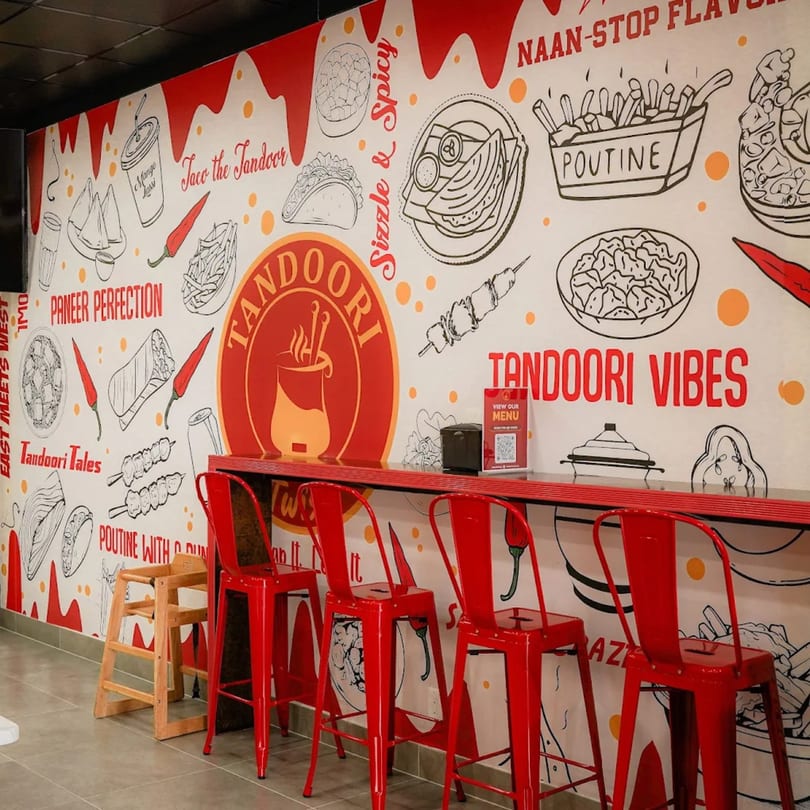A vibrant Tandoori Twist restaurant interior with a food-themed mural and red bar stools.