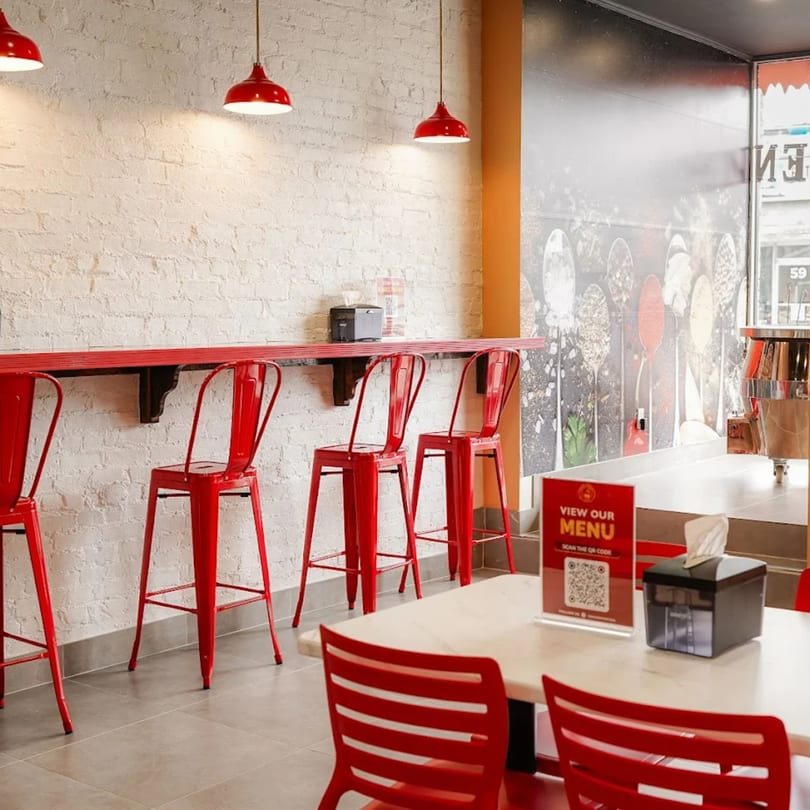 Interior of Tandoori Twist with red bar stools, red pendant lights, and a menu sign on a table.