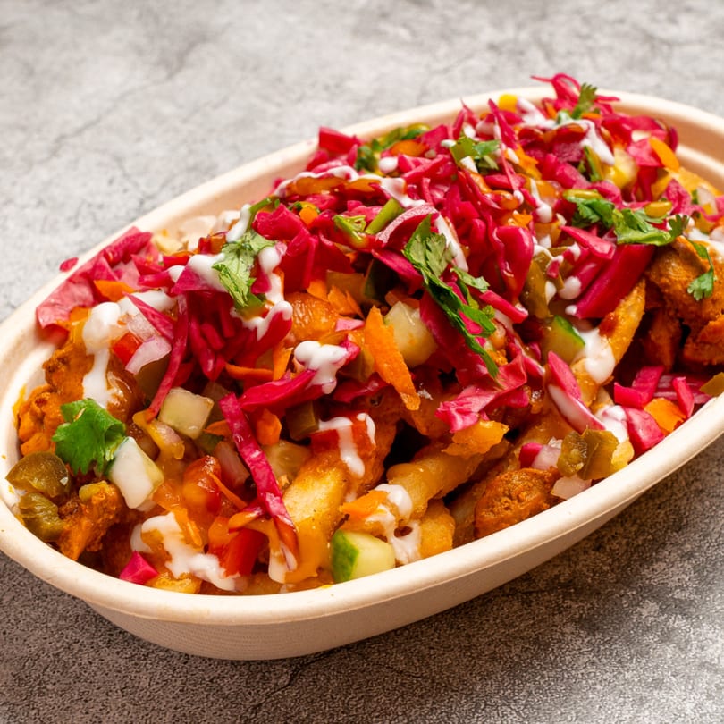 Indian-style loaded fries with red cabbage, cilantro, and white sauce in an oval bowl.