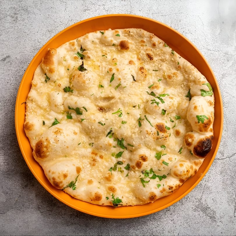 Golden-brown garlic naan bread, garnished with fresh cilantro, served on an orange plate.