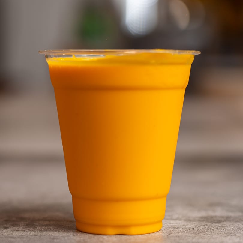 A vibrant orange mango lassi in a clear plastic cup from Tandoori Twist Indian Grub.