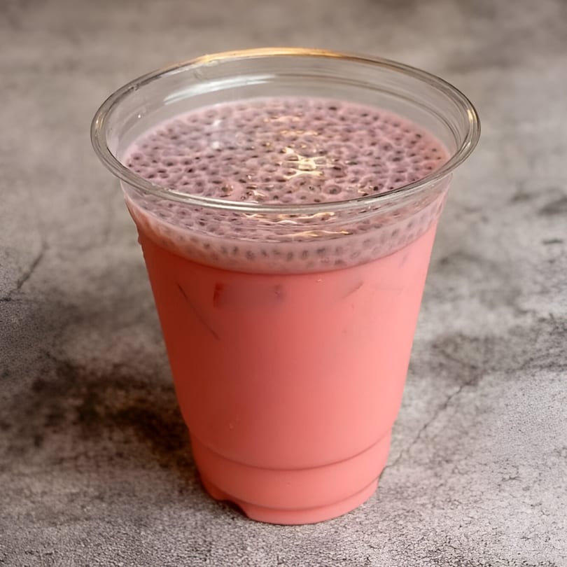 Pink Indian falooda drink with basil seeds in a clear plastic cup on a gray surface.